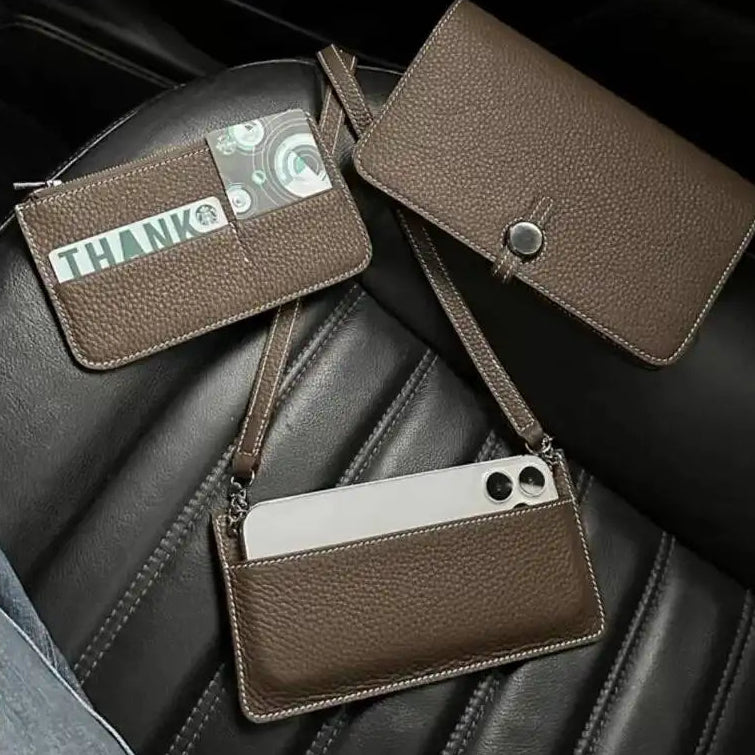 Three brown pebbled leather crossbody phone pouches are arranged on a black car seat. One pouch is open to show card slots with cash and a card, one is closed showing its snap-button closure, and one is open showing a phone inserted into its built-in card holder.
